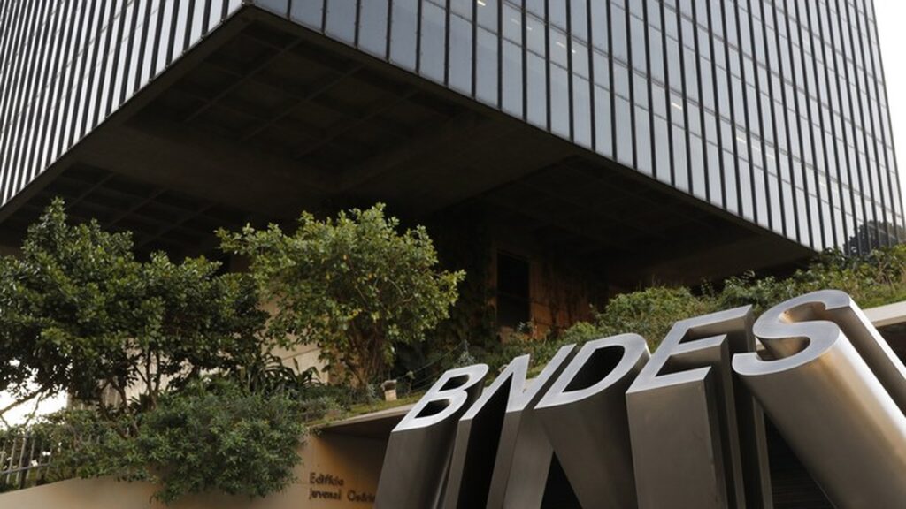 A imagem mostra a sede do BNDES e com árvores na frente
